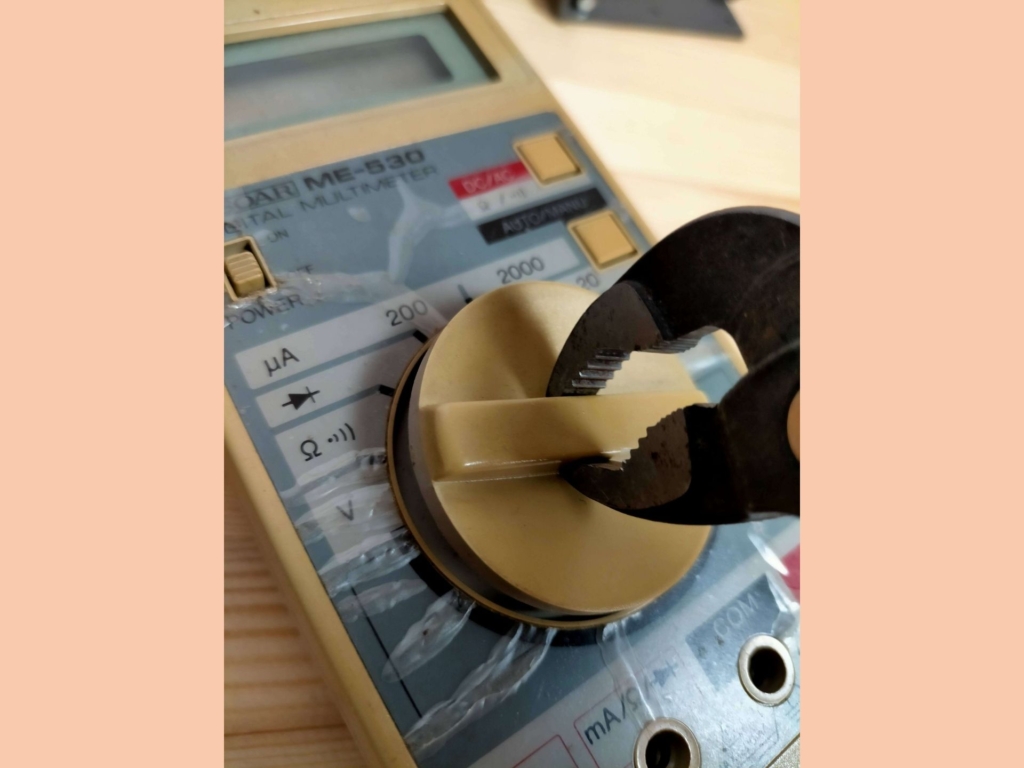 SOAR ME-530デジタルマルチテスターを分解するためにプライヤーでロータリースイッチを慎重に引き抜いている作業