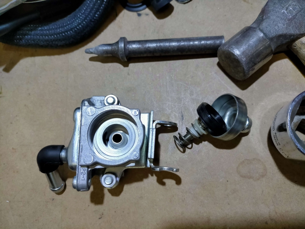 セロー250AISエアカットオフバルブのピストンバルブダイアフラムとエアクリ側からのホースが繋がっていたカバーをポンチで打ち抜いた後・ボディ右側に取り出した部品（ダイヤフラム・圧入カバー）が確認できる状態
