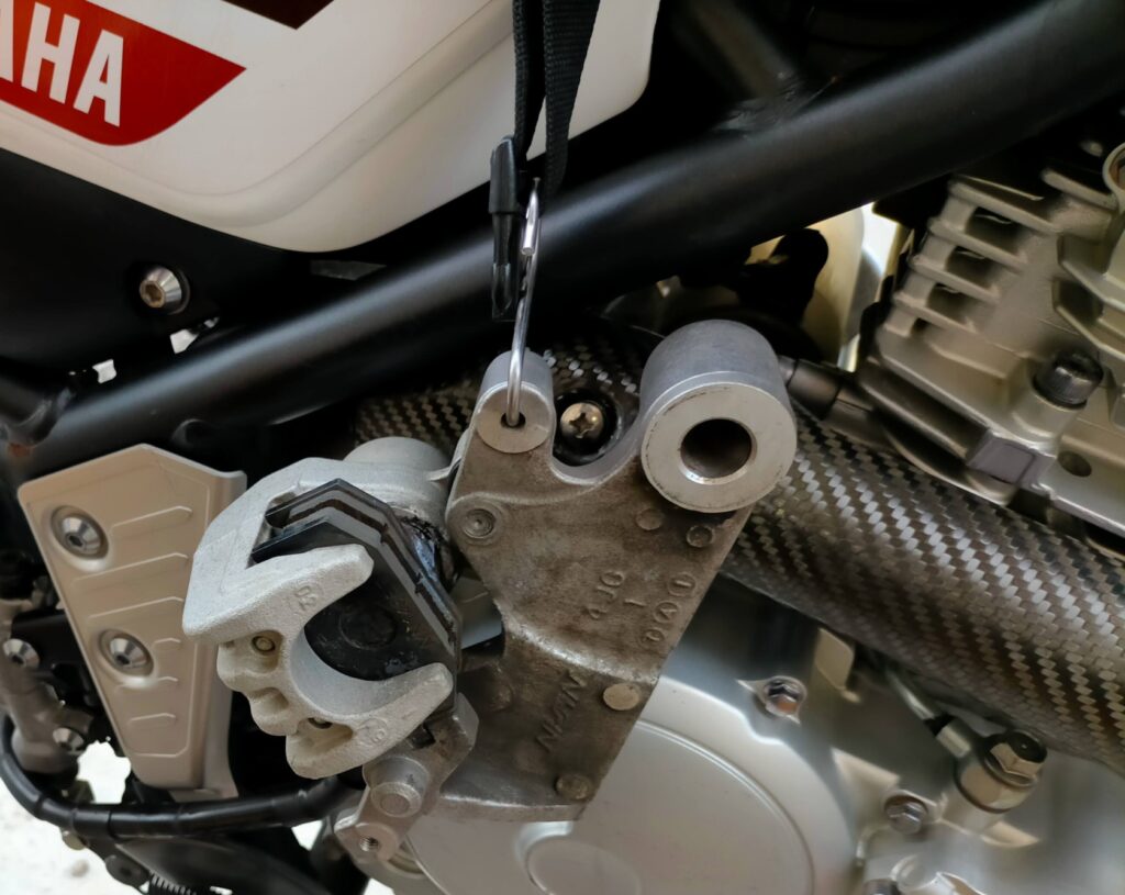 セロー250のリヤホイール取り外し後にリヤブレーキキャリパーをスイングアームから外してフック(ワイヤー等)で吊るし邪魔にならない位置に退避させた状態