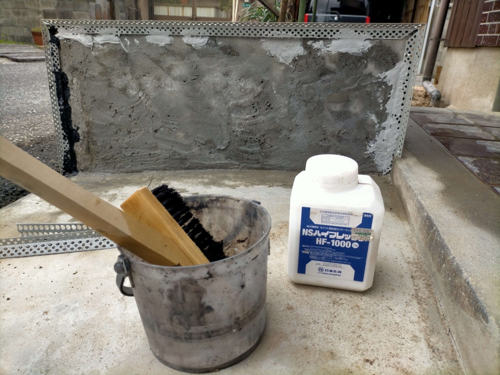 松煙墨モルタル下地の接着強化のためにNSハイフレックスをブラシで花壇ブロック面に塗布する前に水と混ぜている様子(HF1000:水=1:4)