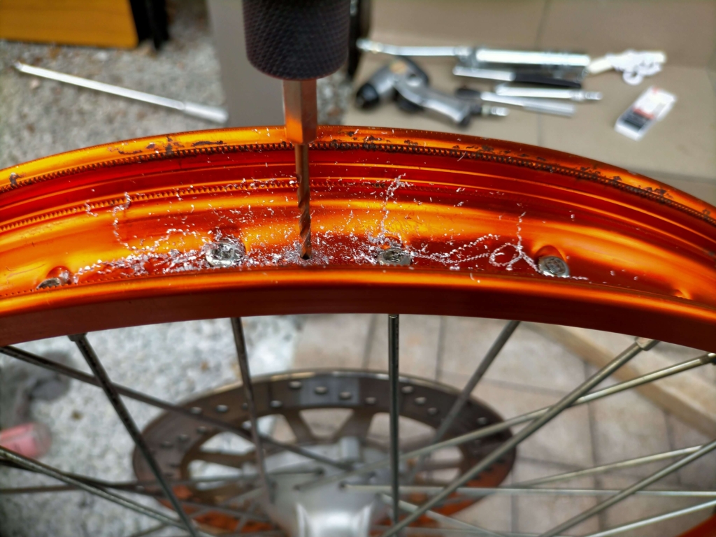 セロー250フロントリムのバルブ穴対角線上にビードストッパー取り付け用の8mm穴をドリルで開けている作業