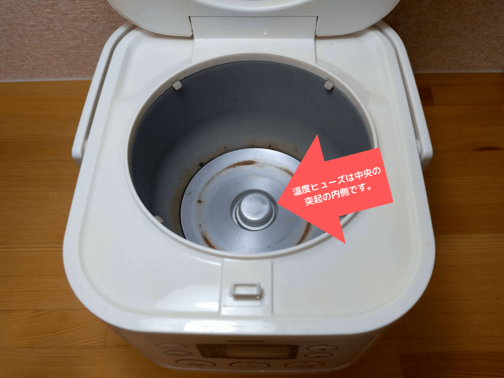 分解前に炊飯器内部の温度ヒューズの位置を矢印で示している様子
