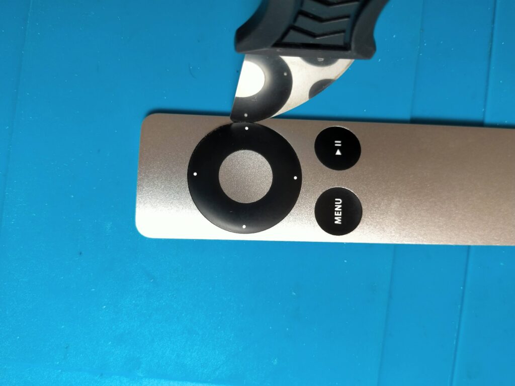 Apple Remoteの上下左右方向ボタンを厚み2.5mmの金属製ヘラでこじって取り外している作業