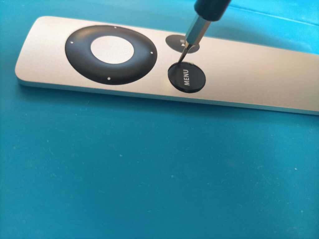 Apple RemoteのMENUボタンの爪横の肉薄部分に1mm幅マイナスドライバーを挿し込んでこじり外している作業