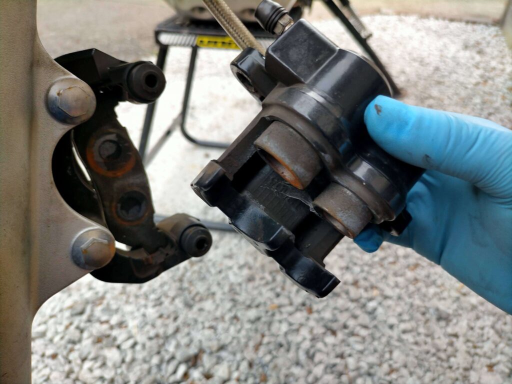 セロー250フロントブレーキキャリパーAssyをブラケットから取り外してブレーキホースを接続したまま吊り下げた状態