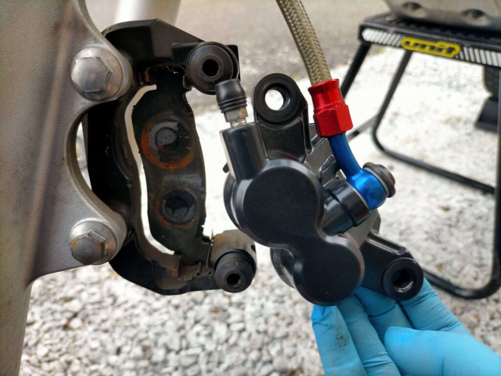 セロー250フロントキャリパーサポートボルト（12mm）を2本取り外してキャリパーをブラケットから分離している作業