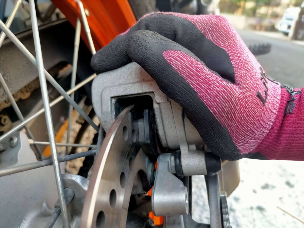 セロー250リヤブレーキキャリパーAssy全体を手でスライドさせてピストンを押し戻しパッドの組み付けスペースを確保している作業