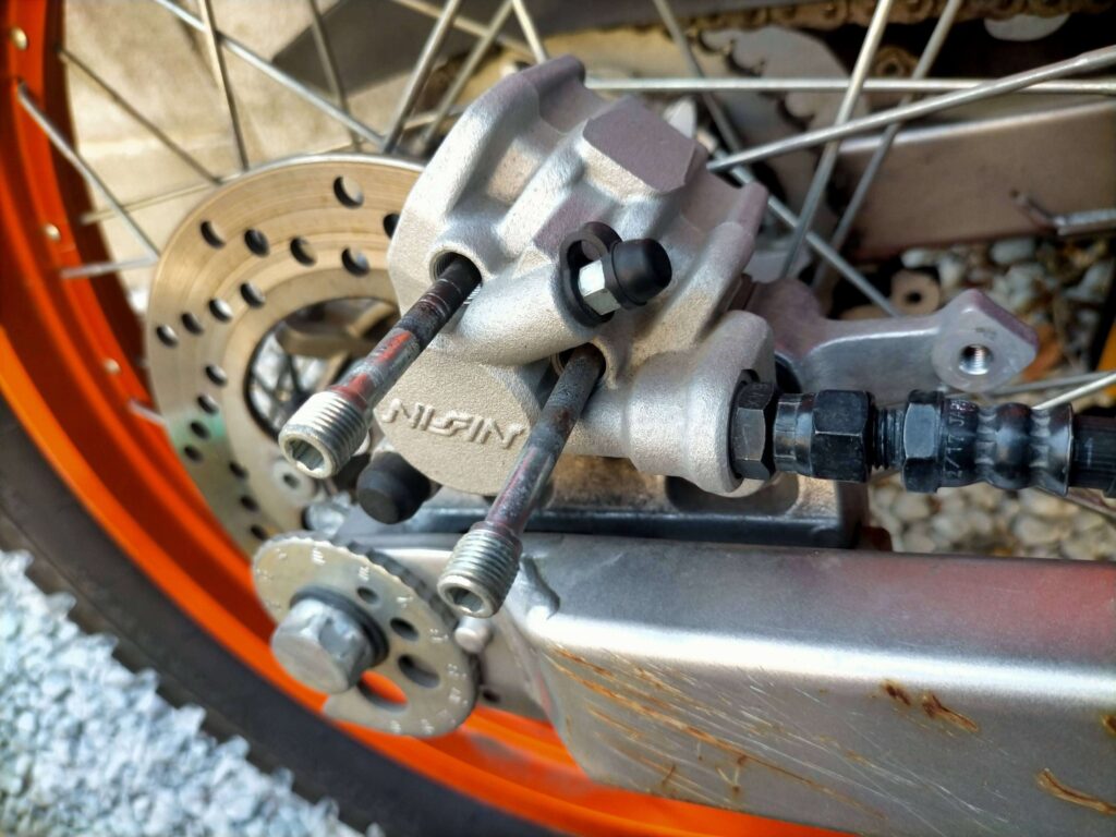 セロー250リヤブレーキキャリパーのパッドを固定するスライドピン兼用サポートボルト2本を5mm六角レンチで取り外している作業