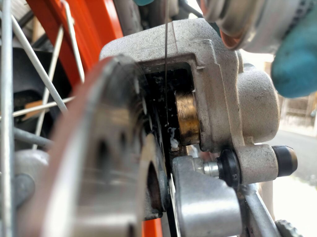 セロー250リヤブレーキのパッドスプリング（リヤキャリパーブラケット側・Assy側）にシリコングリスを塗布している作業