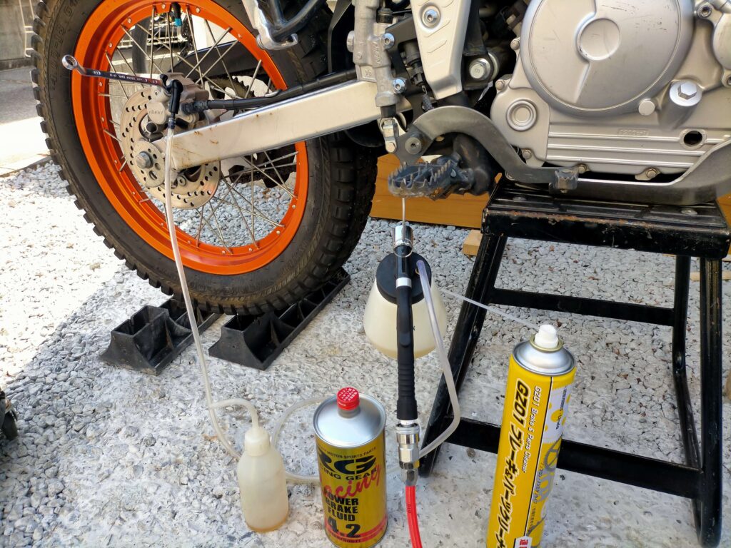 セロー250リヤキャリパーのブリードスクリューに8mmメガネレンチとブリーダーホースをセットしてフルードを排出している作業