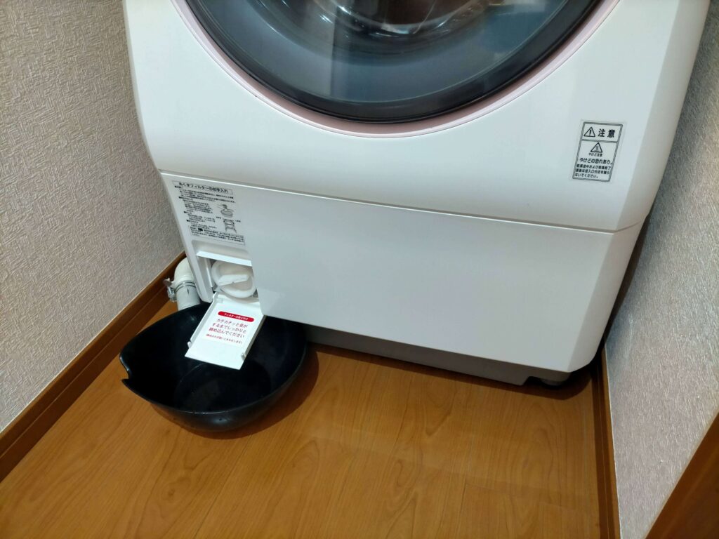 洗濯機の糸くずフィルターを外す前に水受け容器を置く様子