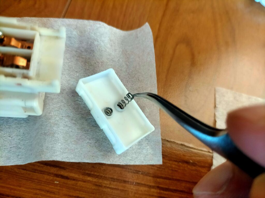 E25キャラバン(いすゞコモ)パワーウィンドウスイッチ清掃後の組み立て作業(スライドパーツにスプリング2つを乗せる)