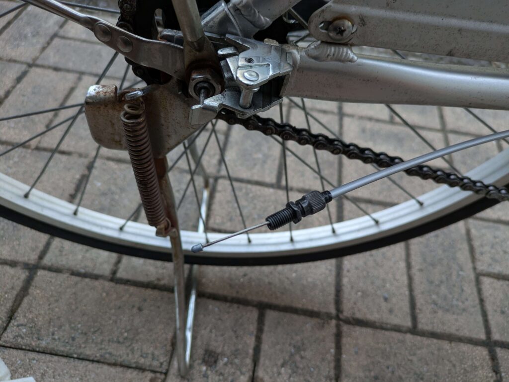 後輪側のケーブル調整ボルトを外す作業（10mmスパナ使用）