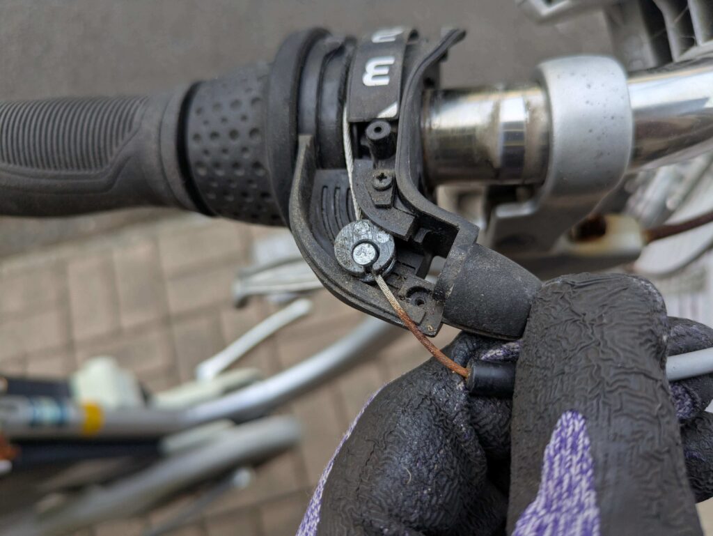 シフトレバーからワイヤーのタイコ（太鼓状金具）を外す作業（1速位置でワイヤー緩む）