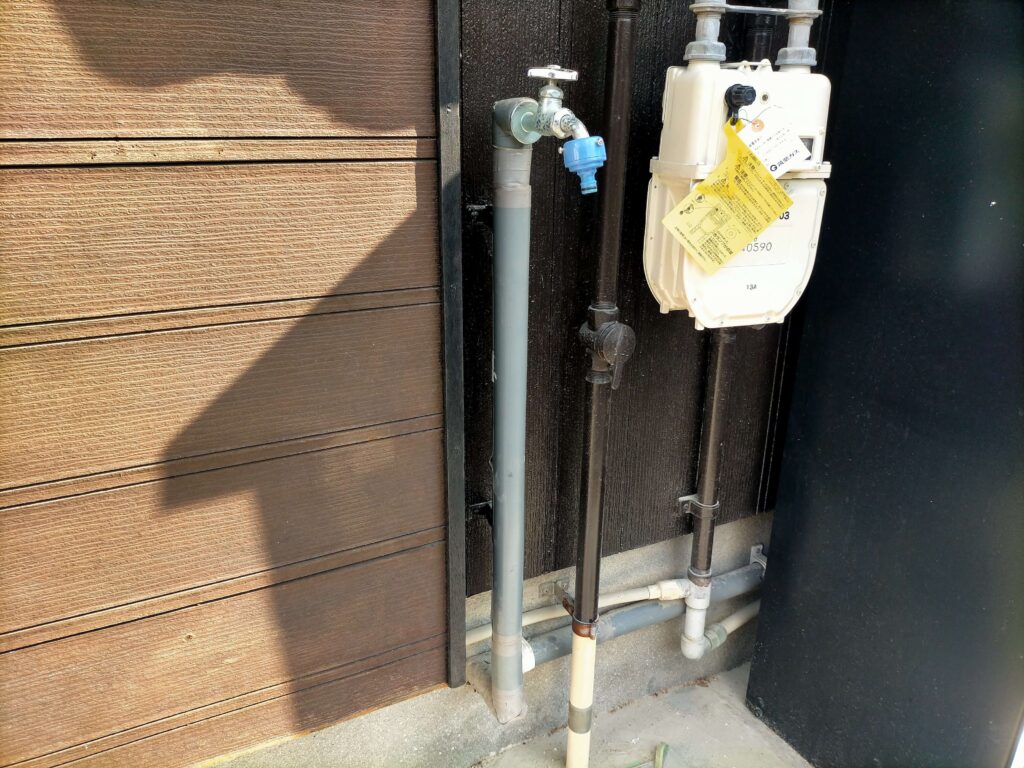 リメイク前の勝手口にある一般的なプラスチック製の立水栓とスポンジカバー