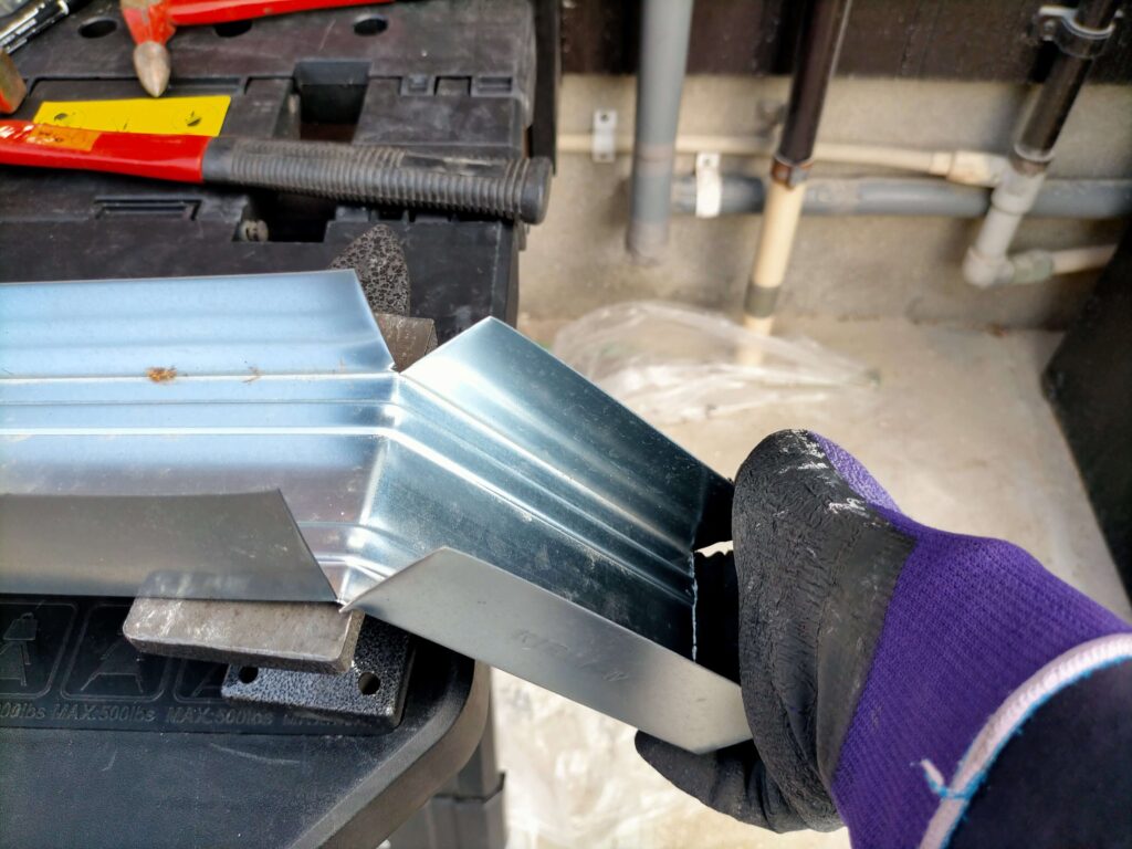 勝手口の立水栓カバーの下端を手で折り曲げ加工している様子