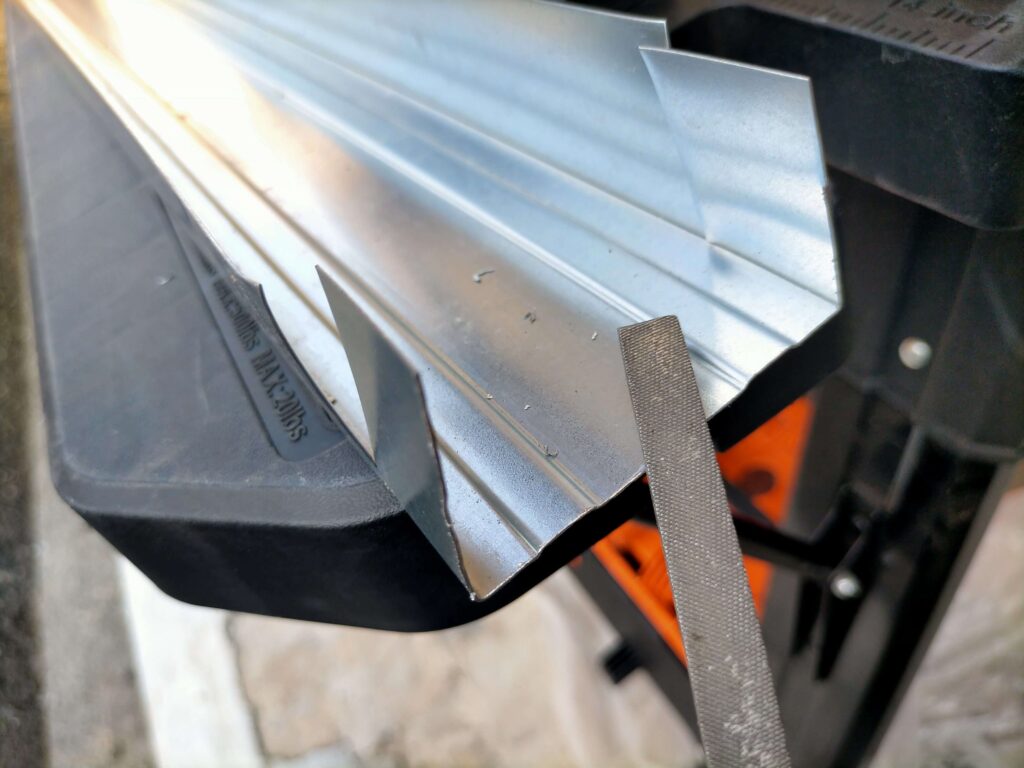 金属の切り口で怪我をしないよう、ヤスリを使って軽天材のバリ取りを行う様子