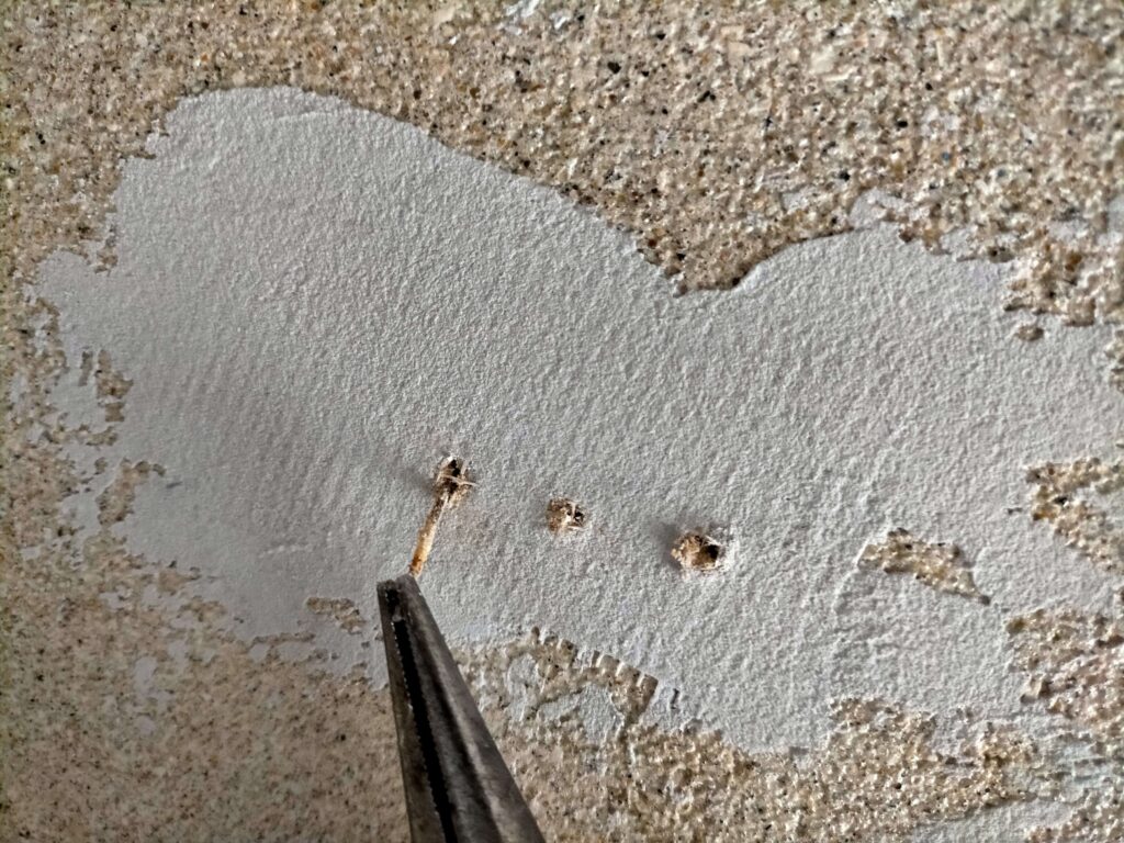 漆喰アンダーコートの表面に錆色が浮き出た所から古釘をラジオペンチで抜いている様子