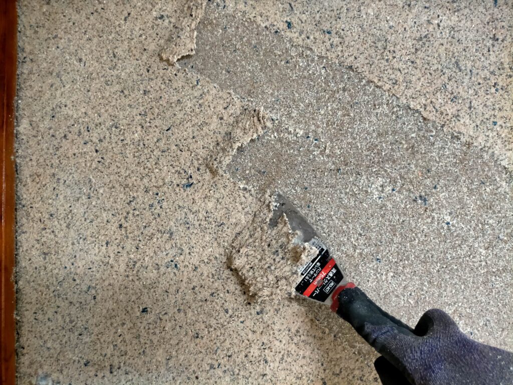 水を含んでふやけた繊維壁をスクレーパーを使って下地の砂壁から綺麗に剥がす作業