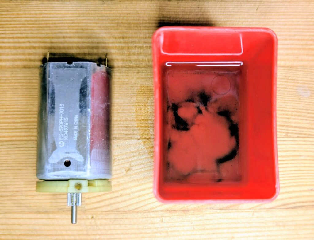 モーターのブラシ・整流子部分から出てきたカーボン汚れがIPA（イソプロピルアルコール）容器の底に溜まっている様子