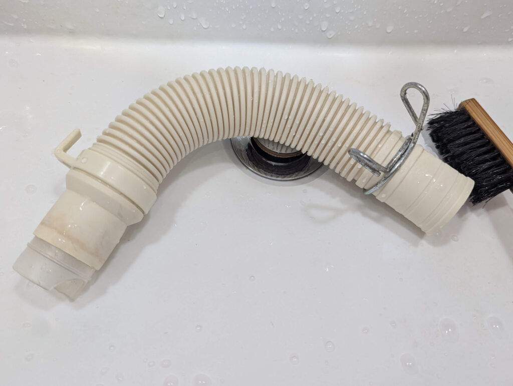 取り外した排水ホースの中に水を流し込み、内部の詰まりや汚れを洗い流す掃除の様子