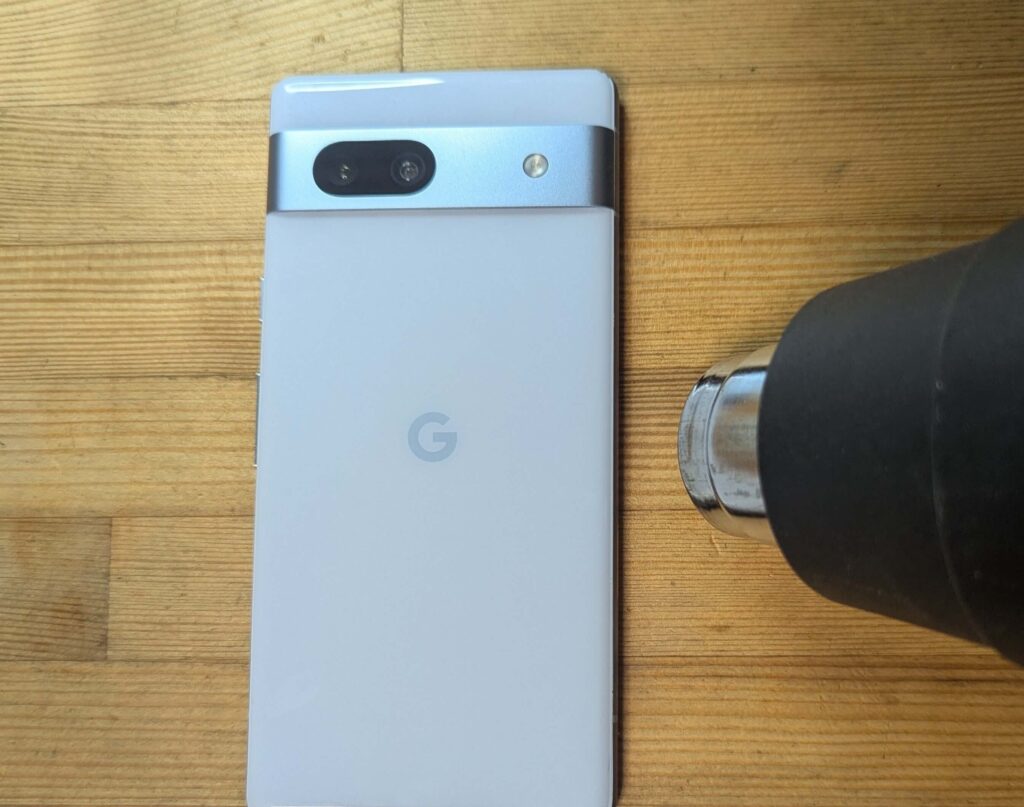 強力な接着剤を緩めるためにヒートガンでGoogle Pixel 7aの背面パネル外周を温める様子