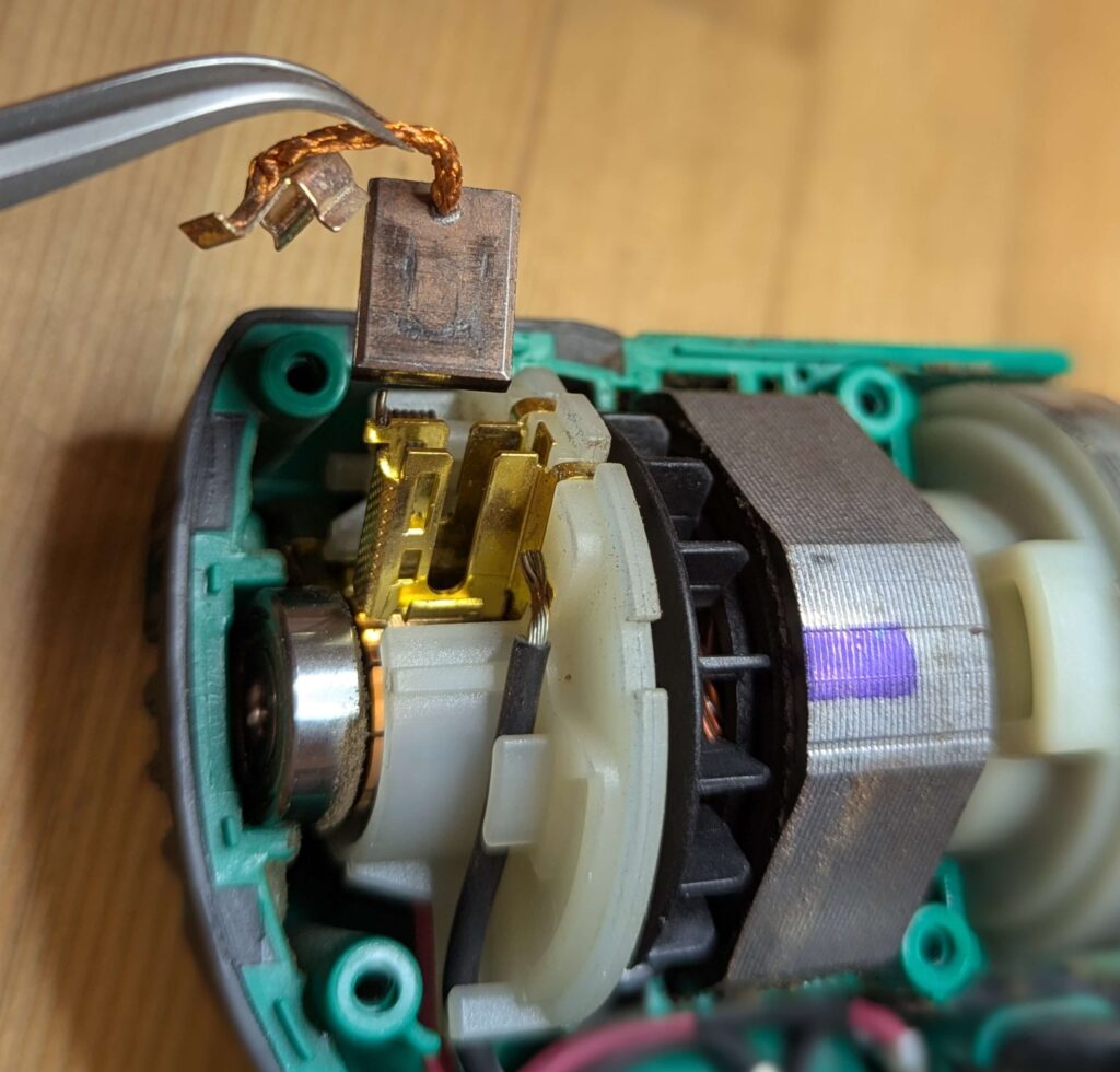 摩耗した古いカーボンブラシをホルダーから引き抜いて取り出す様子