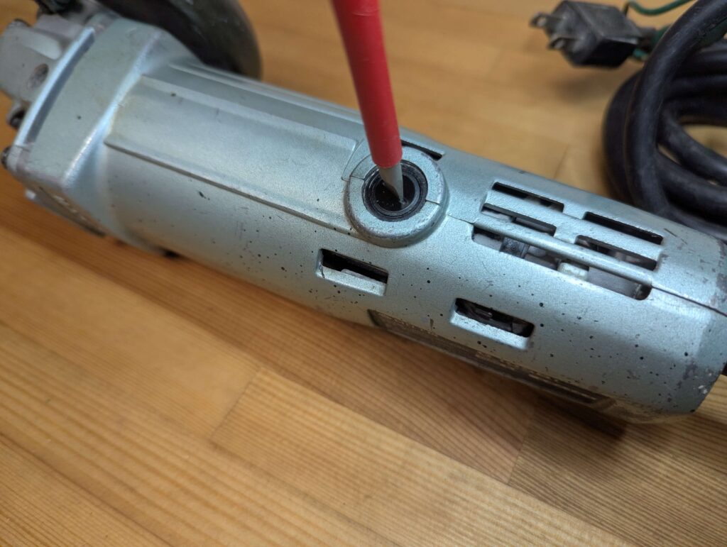 マイナスドライバーを使ってディスクグラインダーのカーボンブラシキャップを取り外す様子