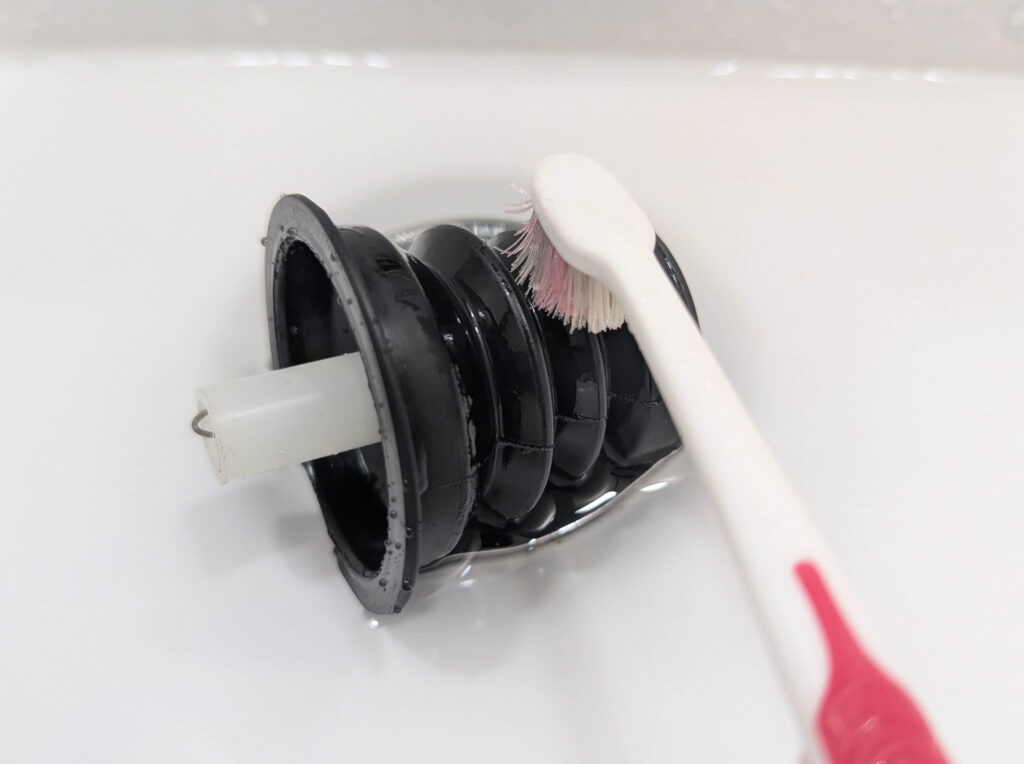 排水弁のゴムパッキンを歯ブラシで丁寧に清掃する作業