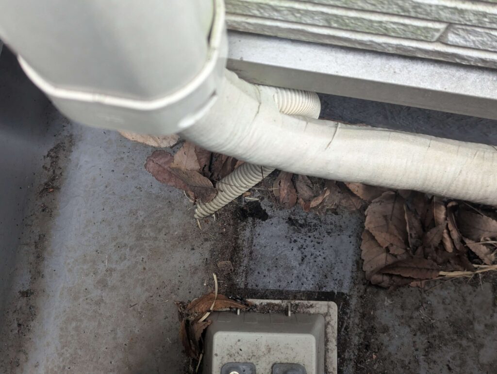 家庭用エアコンのドレンホース（室外）を地面に設置しているので枯葉に埋もれている様子