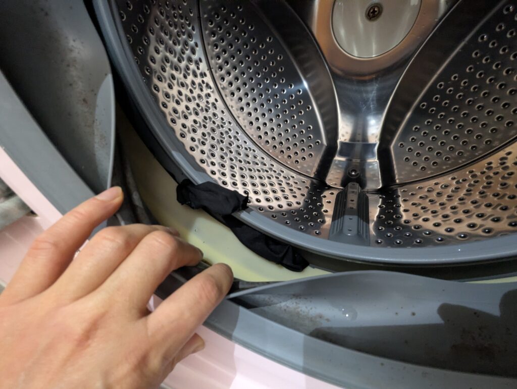 ドラム式洗濯機のドアパッキン（ゴムシール）裏に溜まった黒カビと洗剤カス。黒いワカメ基本診断Step3の確認箇所。月1回の拭き取り・カビキラーによるカビ除去→槽洗浄コースで解決できる場合がある。工具不要で確認できる最重要チェック箇所