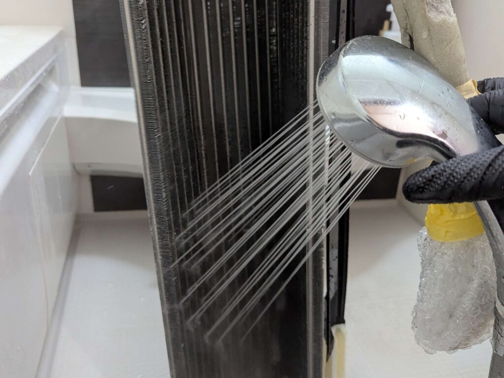 フィンの洗浄液をシャワーのお湯で流している作業