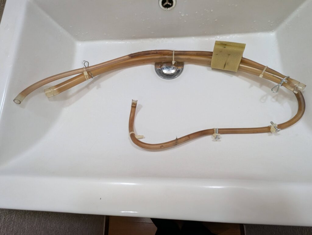 東芝 TW-160SCH ドラム式洗濯機から取り外した循環ホース(太)と濃縮バブル洗浄用(細)ホースの洗浄中。チューブブラシでブラッシング後にエアで吹くと柔軟剤・洗剤カスのヘドロ状固形物が大量に排出された。洗剤液循環経路(糸くずフィルター→循環ポンプ→ホース→槽内シャワー)の清掃