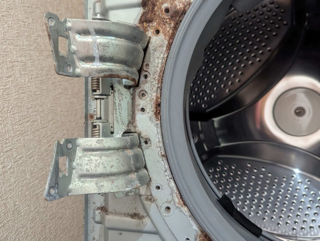 東芝 TW-160SCH ドラム式洗濯機の洗剤投入口下の前面パネル・ドアパッキン押えプレート・メッキのドアヒンジに発生した腐食と白粉吹きの状態。洗剤投入口下は特に腐食がひどく、19年分の洗剤飛沫と湿気による経年腐食の発見