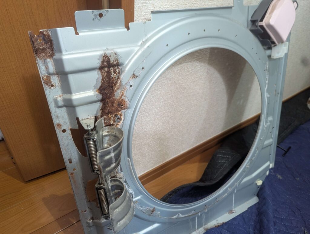 東芝 TW-160SCH ドラム式洗濯機の洗剤投入口下の前面パネルのサビ取り前(Before)。洗剤飛沫が繰り返し付着して特にひどい腐食状態。ワイヤーブラシでの研磨→サビキラープロ塗布による防錆修復前