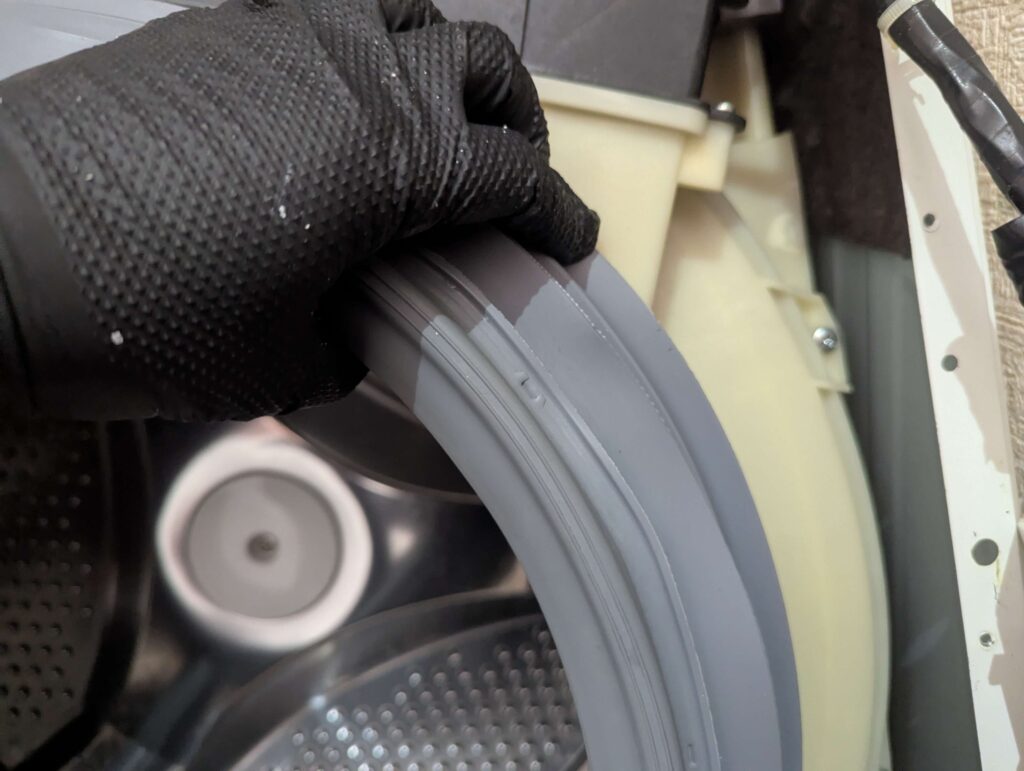 東芝 TW-160SCH ドラム式洗濯機の外槽前カバーにドアパッキンを合いマークを合わせてはめ込んでいる状態。シリコンシーラント塗布後・スプリングワイヤー取り付け前。位置ズレによる水漏れを防ぐために合いマークの照合が必須