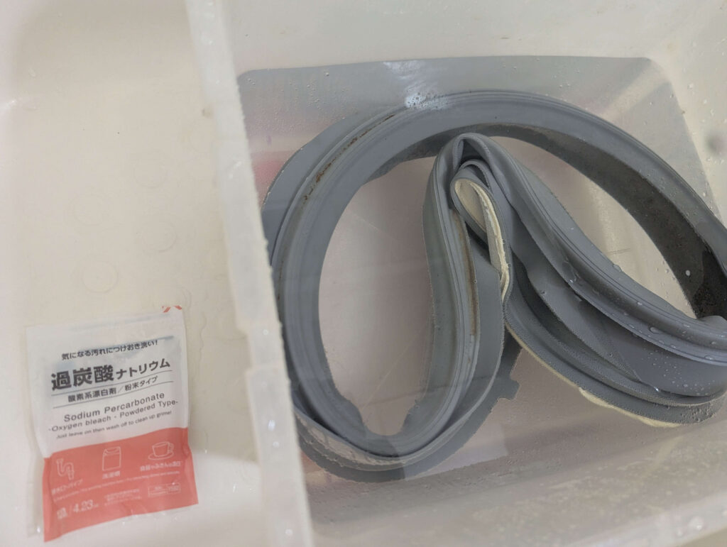 東芝 TW-160SCH ドラム式洗濯機から取り外したドアパッキン(ゴムシール)を過炭酸ナトリウム温水に一晩漬け置き洗浄している状態。カビ・洗剤カスを酸素系漂白剤で浮かせて除去する前処理。19年使用のパッキンだが弾力が維持されていた