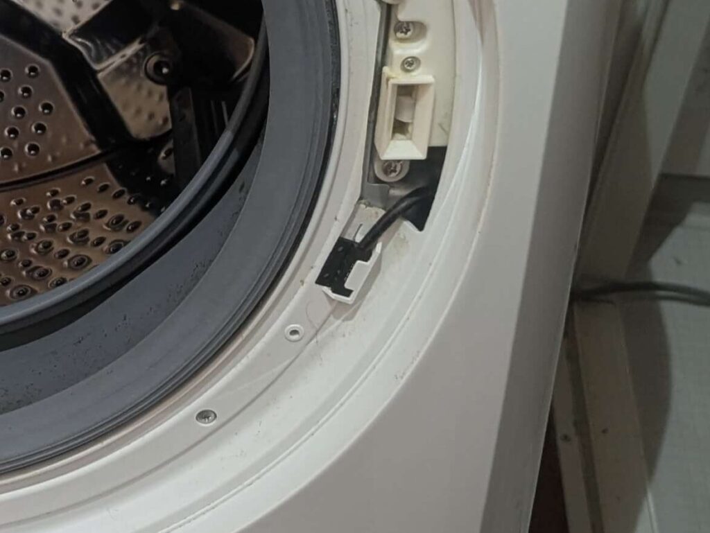 東芝 TW-160SCH ドラム式洗濯機の前面カバー(大)にはめ込まれているドア開閉確認用の磁気センサー。前面カバー取り外し時に忘れず取り外す必要があるパーツ。見落として前面カバーを引き抜くとコネクター・ハーネスが断線するリスクがある