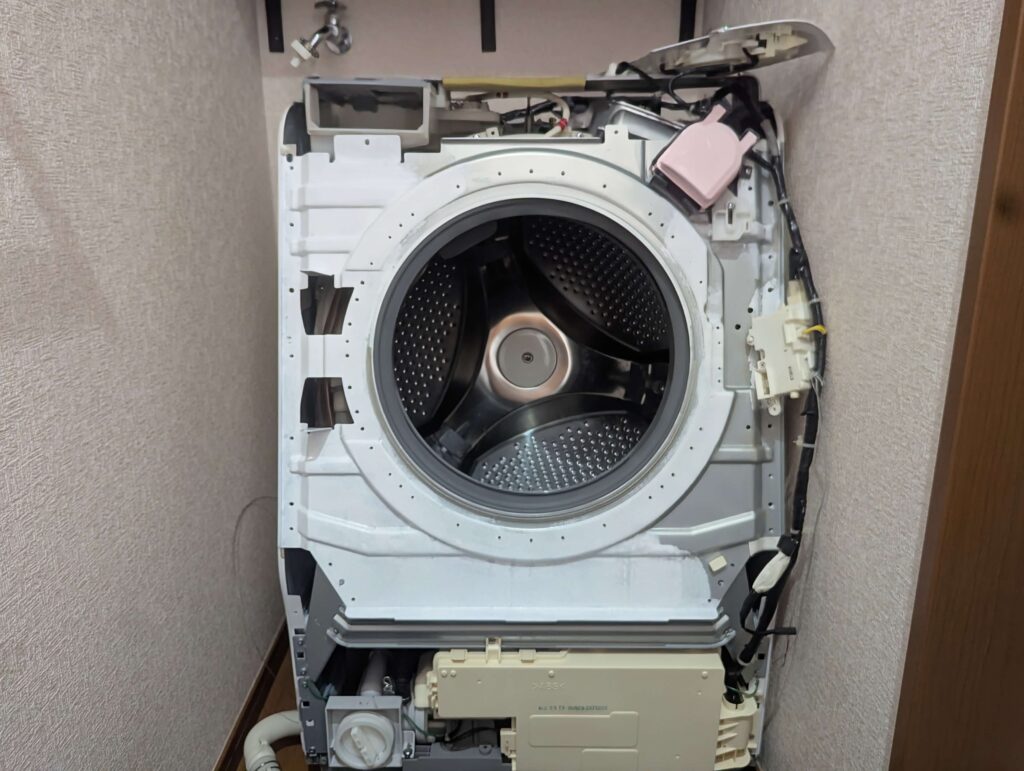 東芝 TW-160SCH ドラム式洗濯機の前面板金パネルを取り付けてドアラッチと配線ケーブルを接続している状態。分解と逆の手順での再組み付け。ラッチのフックとケーブルコネクターの接続を確認してから固定ネジを締める