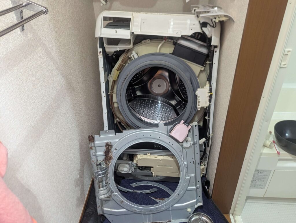 東芝 TW-160SCH ドラム式洗濯機の全面板金パネルをドアラッチ・配線ケーブルとともに取り外した状態。外槽前カバーへのフルアクセスが可能になった状態。Step1・外装カバー完全分解完了