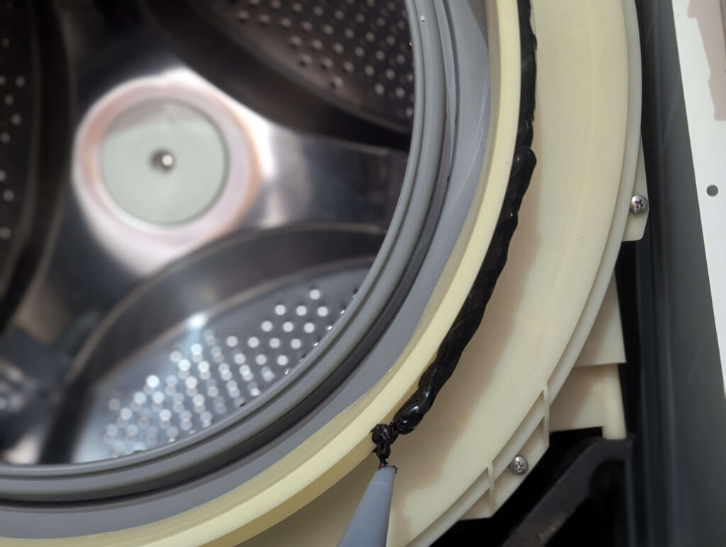 東芝 TW-160SCH ドラム式洗濯機のドアパッキン取り付け箇所(外槽前カバー)にシリコンシーラントを塗布している状態。水漏れ防止のための元来の処置を再現。合いマークに合わせてパッキンをはめ込む前の工程