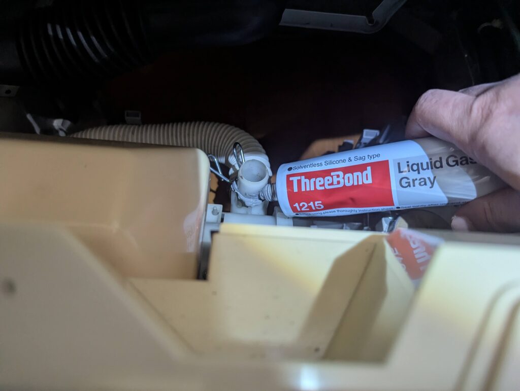 東芝 TW-160SCH ドラム式洗濯機の排水ホース接続部にスリーボンド液状ガスケット(TB1215)を塗布している状態。外槽前カバーの再取り付け時に水漏れを防ぐための液状ガスケット施工。竹串で均一に塗り広げる方法