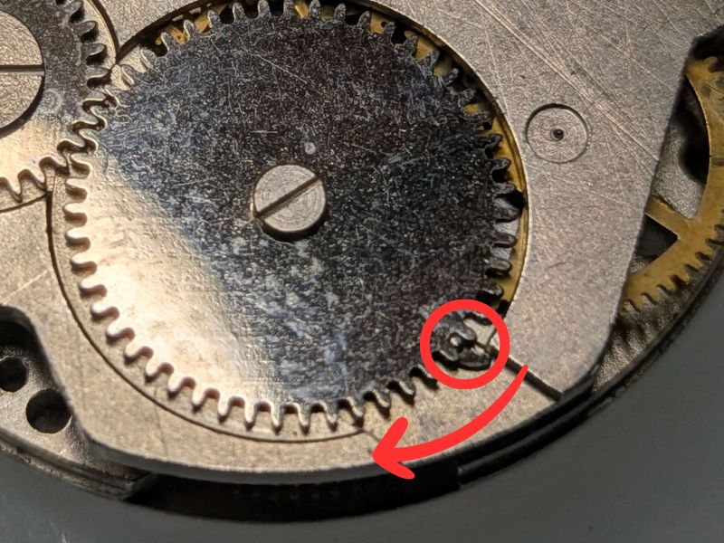 BRADLEY社製ミッキーマウス首振り腕時計の香箱の上にある角穴車の歯に噛み合っているこはぜをスライドさせて解除する方向を示す図