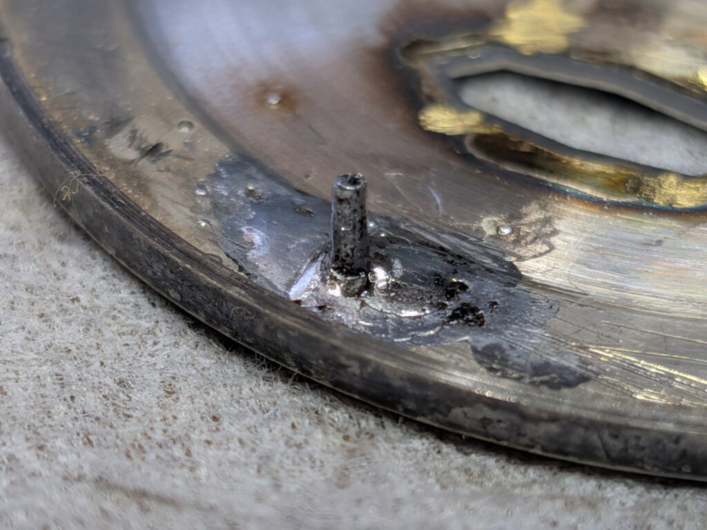 衝撃で折れた干支足(文字盤の足)のハンダ付け修復が完了した接合部分を示す、シチズン・クリスタルセブン27石の文字盤裏面のマクロ拡大写真