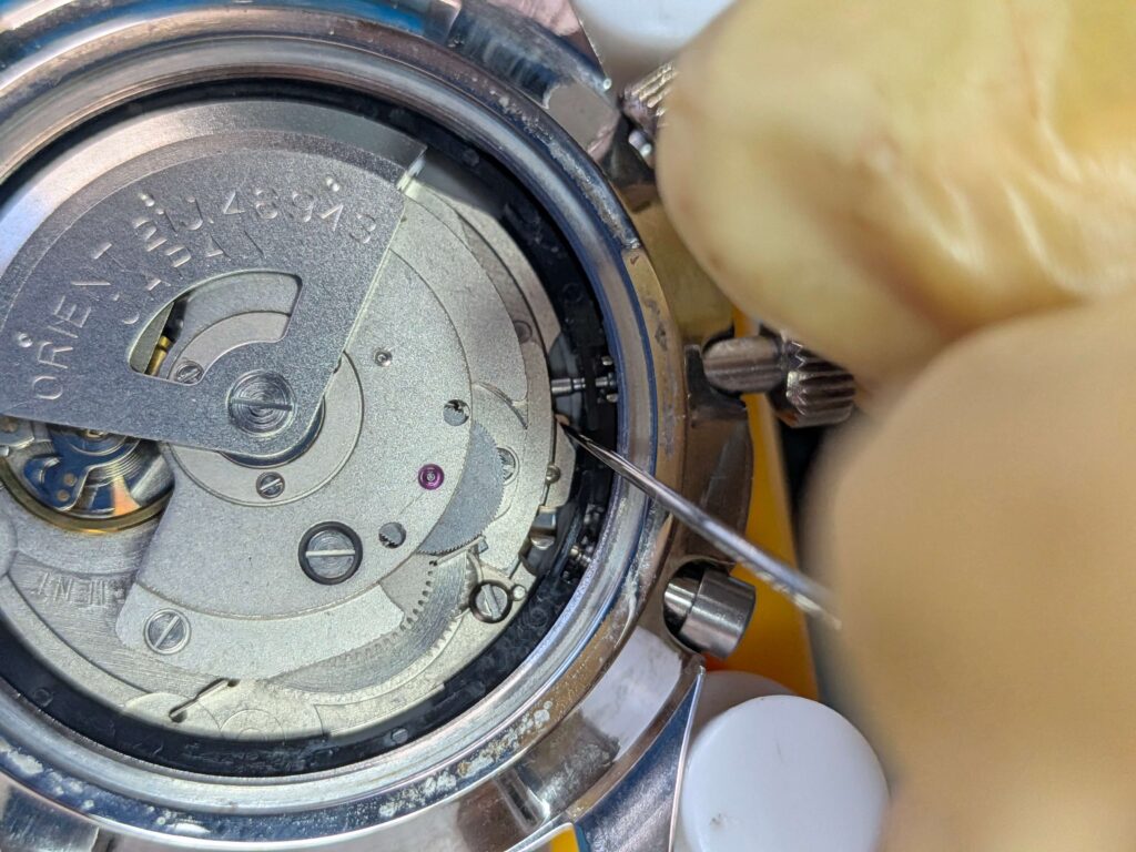 針でオシドリを押しながらオリエント・キングマスター(EM00-C2)のリューズ(巻き芯)を引き抜く様子