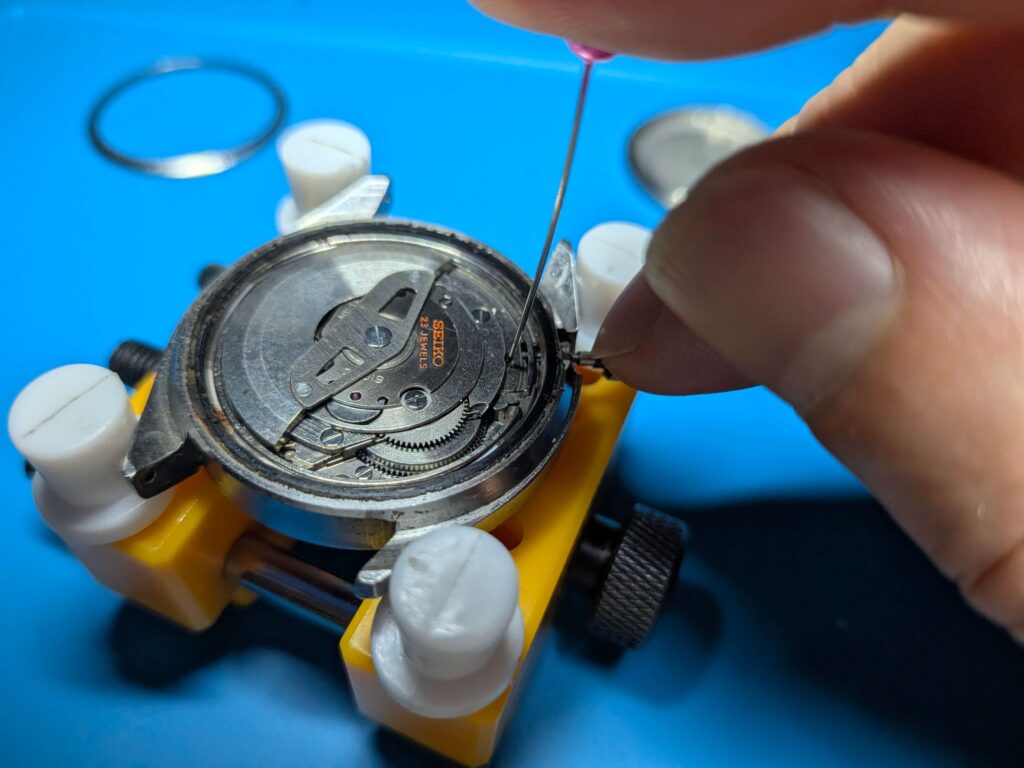 ピンや工具でオシドリを慎重に押し下げながらセイコー5アクタスのムーブメントから巻真とリューズを引き抜いている様子