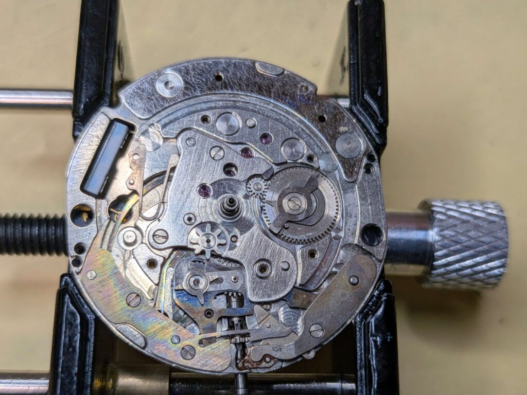 押さえ部品が外され、裏回りの歯車列や巻真周りが露わになった時計ムーブメント