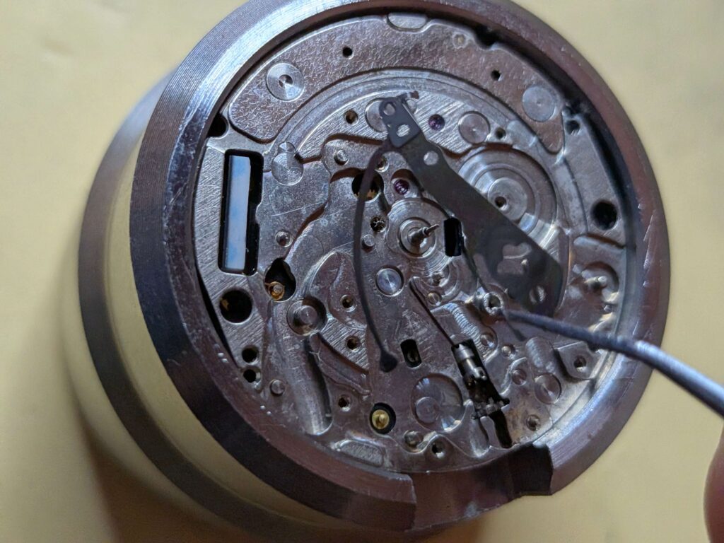 ピンセットを使用してムーブメントから押さえ板（カバープレート・バネ部品）を取り外す様子