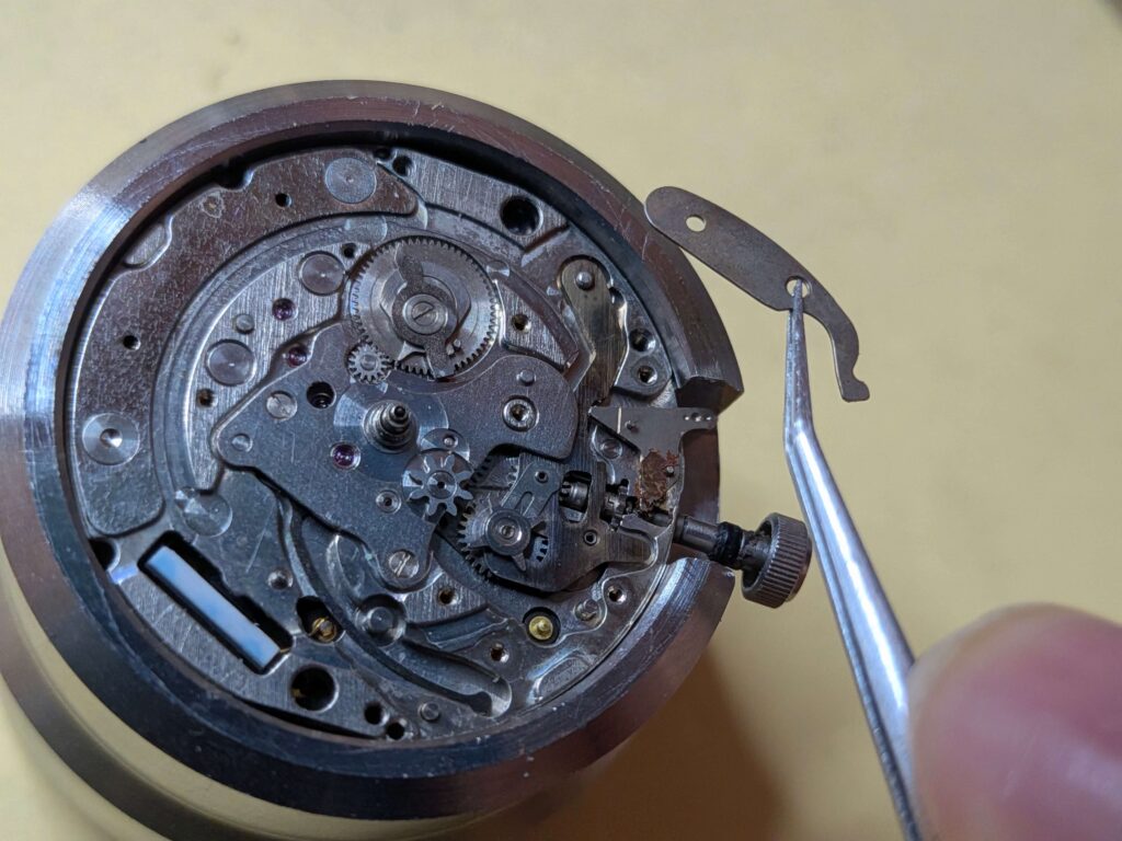 ムーブメントの外周にある細長い板バネ状の部品をピンセットで取り外す作業