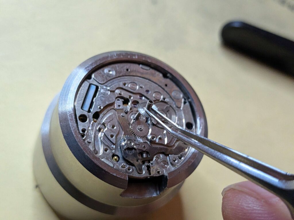 ムーブメントの中心軸から、筒状の歯車（筒カナ）をピンセットで慎重に引き抜く作業